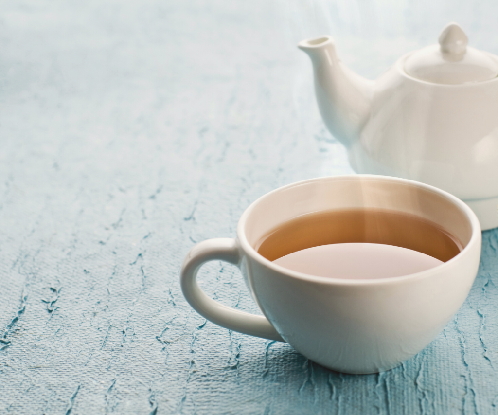 Picture of white teapot and teacup filled with tea in a light blue background.
